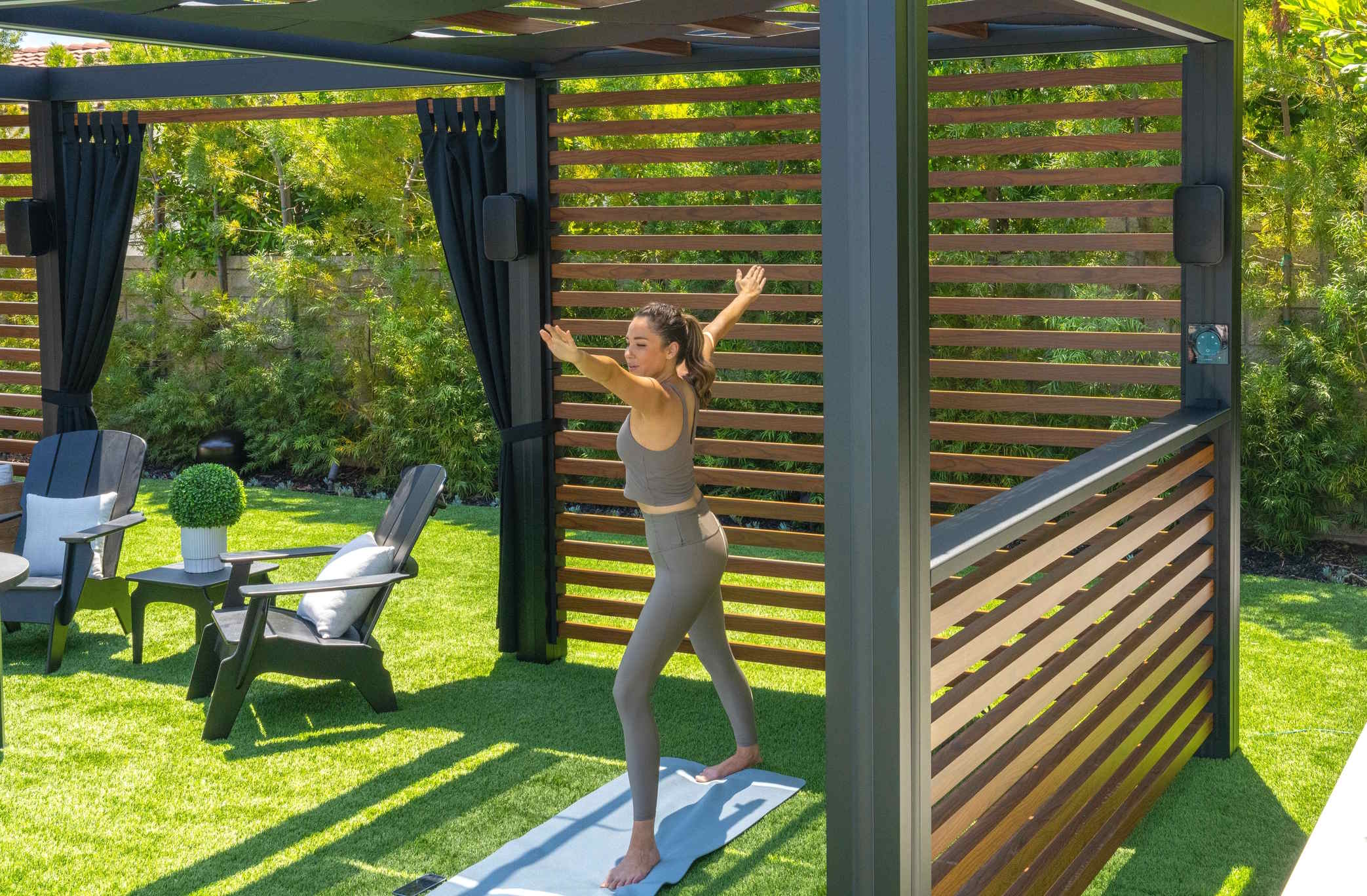 Outdoor pergola with a person stretching on a yoga mat surrounded by greenery.