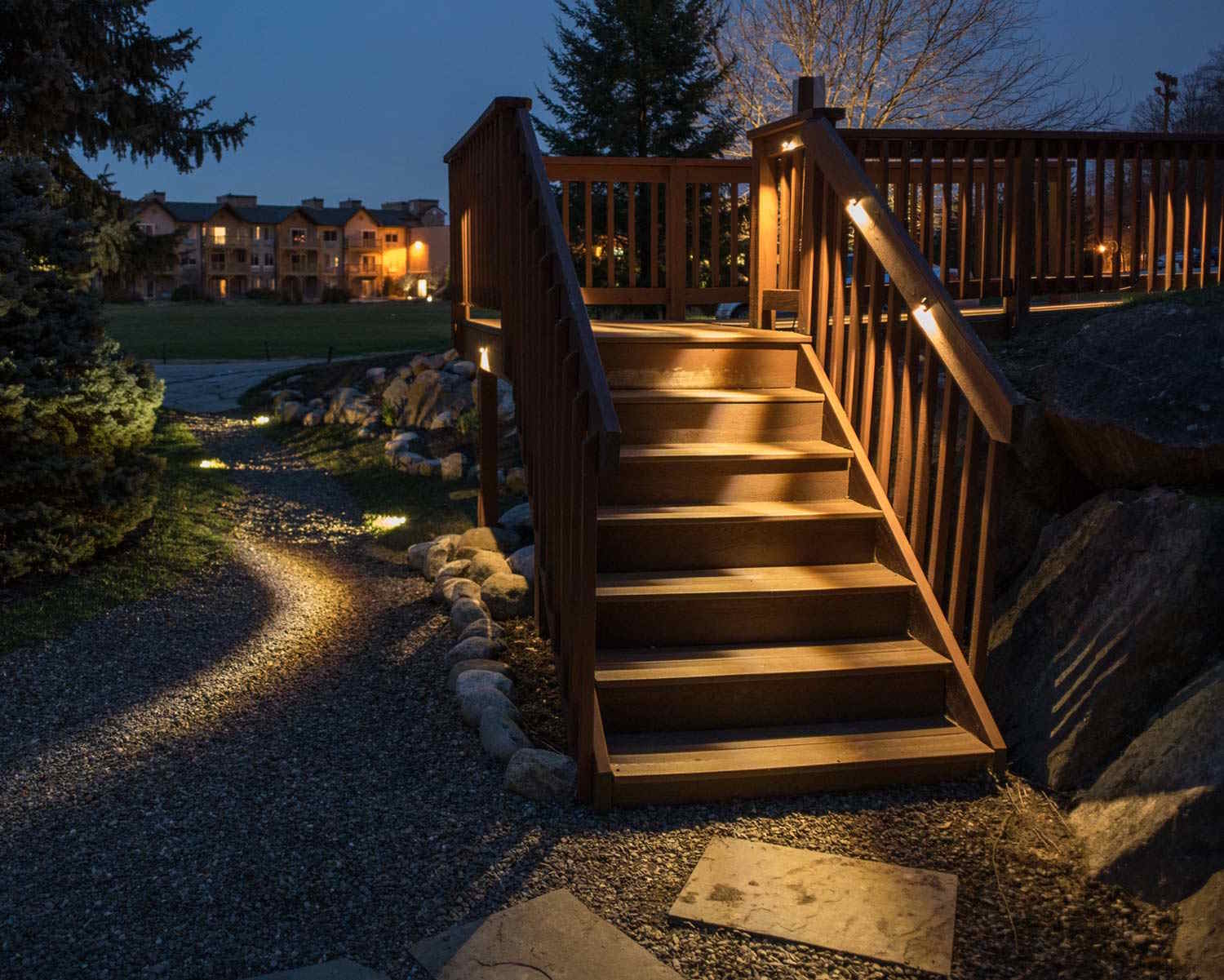Outdoor wooden staircase lit with warm step and railing lights leading to a deck at dusk.