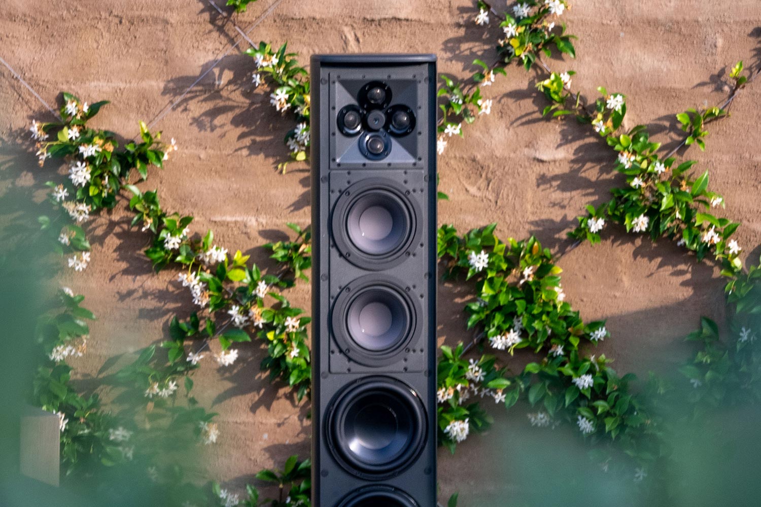 Tall black tower speaker mounted against a stone wall with vines