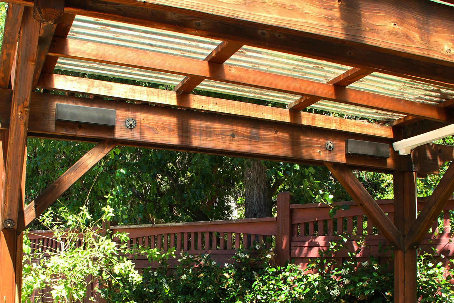 Dark rectangular speakers mounted on the support beams of a wooden pergola