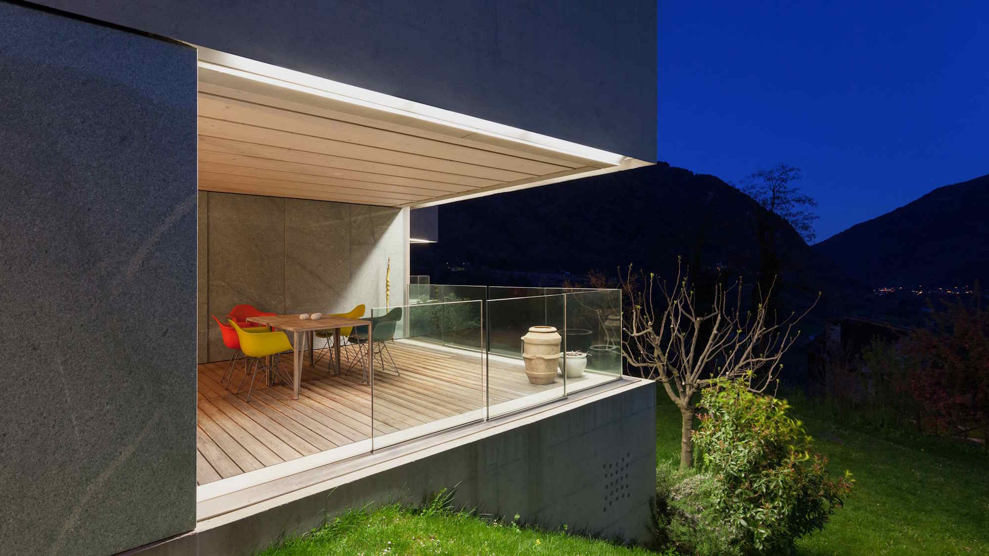 Modern terrace with wooden accents, colorful chairs, and a nighttime mountain view.