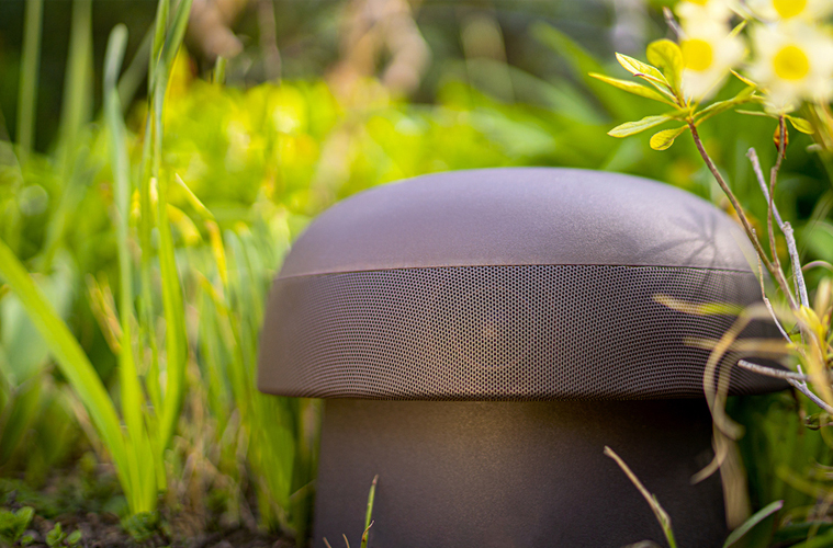 Outdoor mushroom‑style speaker nestled among plants and flowers.