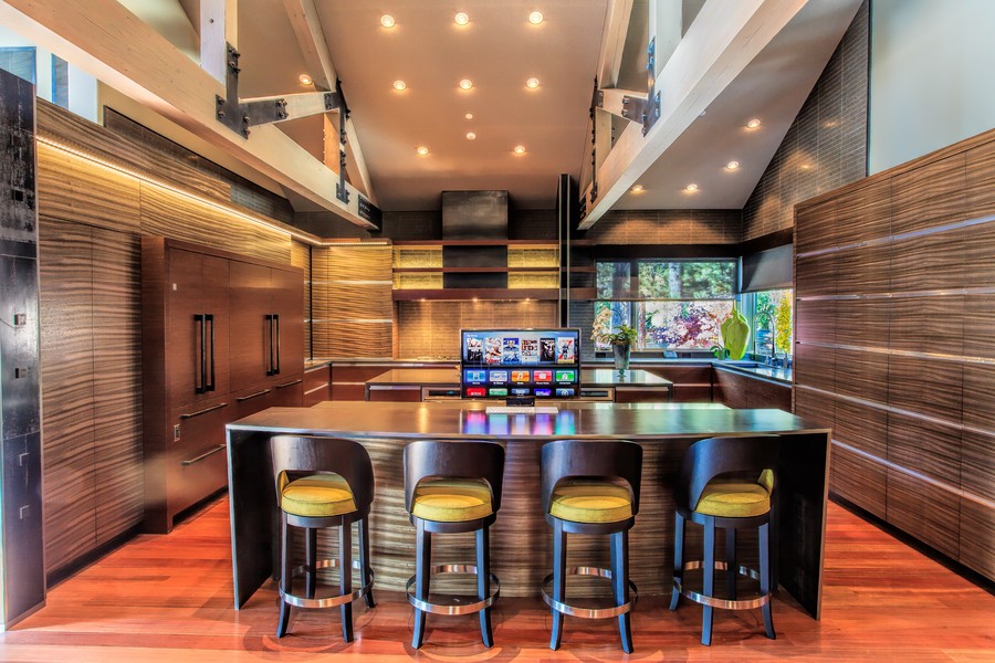 kitchen island with four barstools overlooking a TV rising out of it. Windows with shades are in the background.