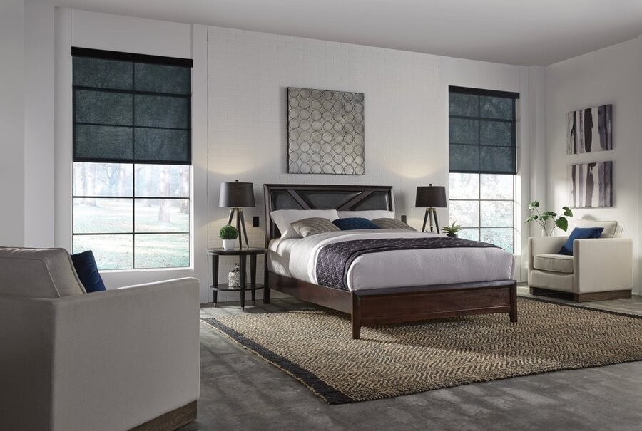 A bedroom with two windows on either side of the bed, with motorized shades lowered halfway down on each.