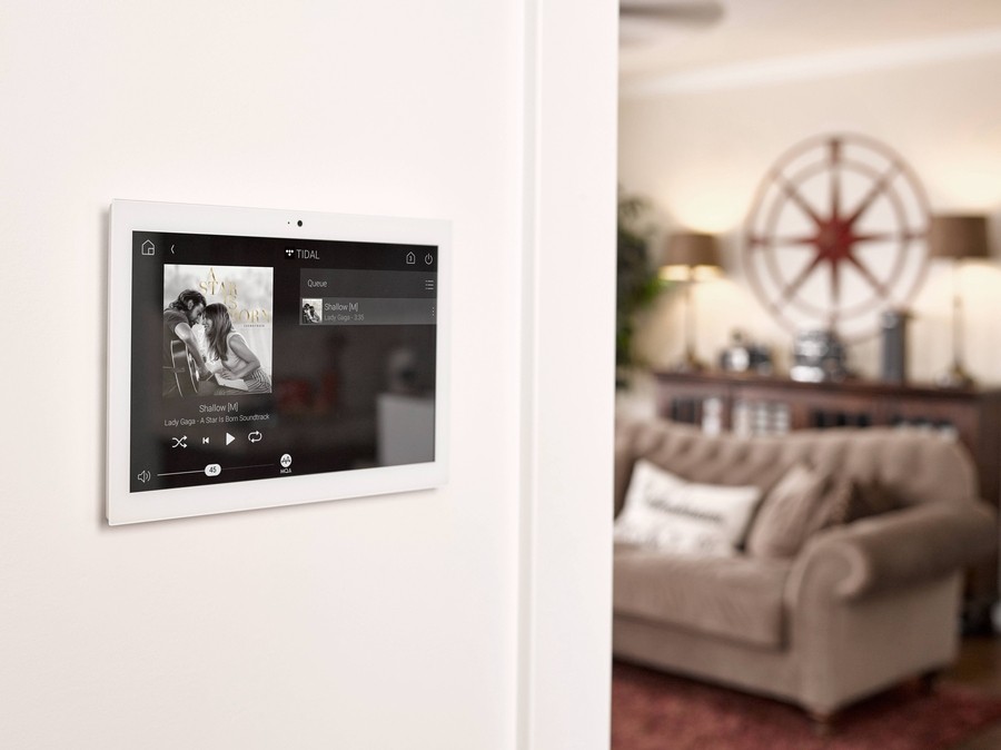 A wall-mounted tablet with the Control4 audio-video interface displaying the A Star Is Born album artwork. 