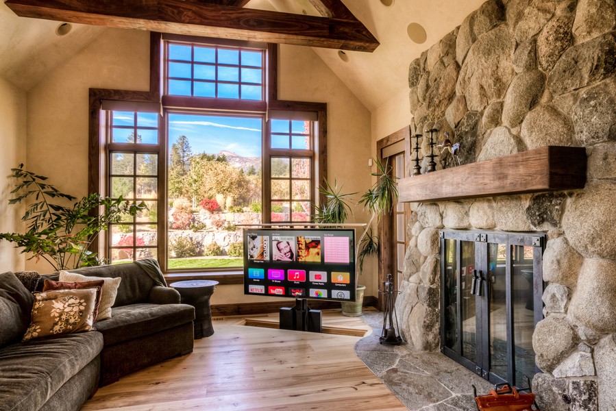 Rustic living room with large window view, fireplace, and motorized TV lifting from floor.