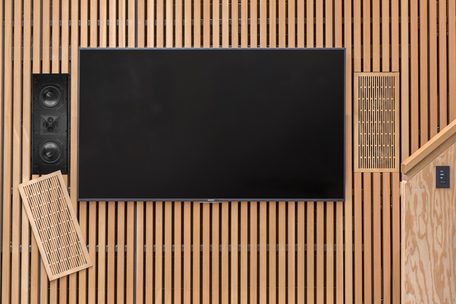 A flatscreen TV on a wood-paneled wall with two in-wall speakers on either side.
