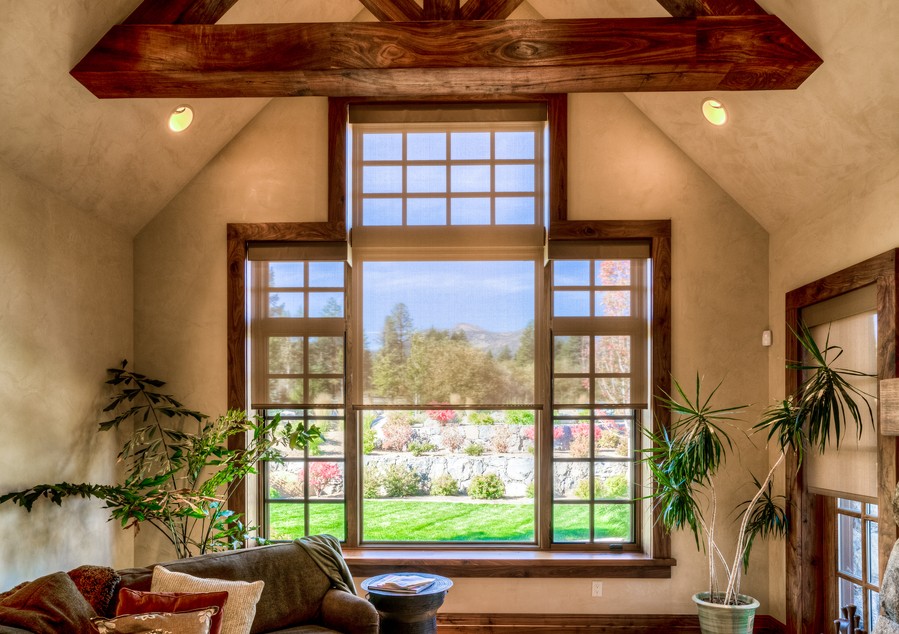 Large living room window with partially lowered automated shades, wood trim, and scenic yard view.
