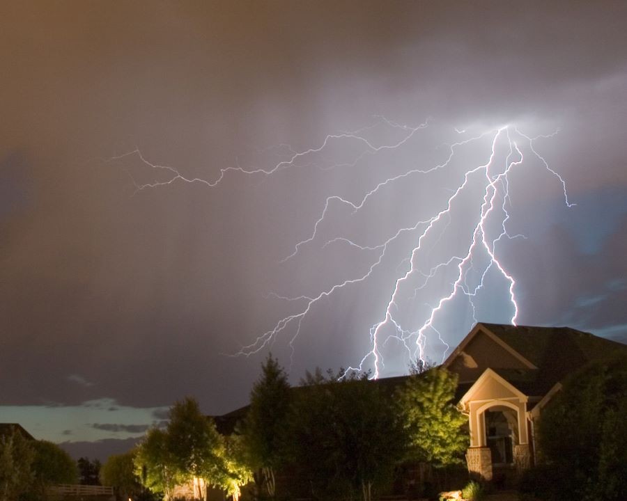 A large lightning bolt lighting up the sky behind a house.