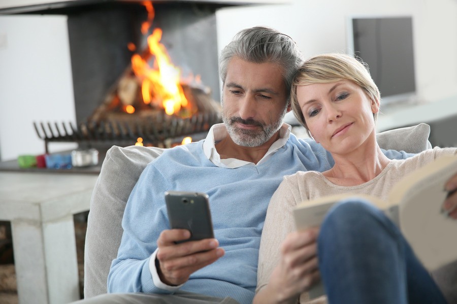 Couple sitting together on the couch looking at their smartphones. 
