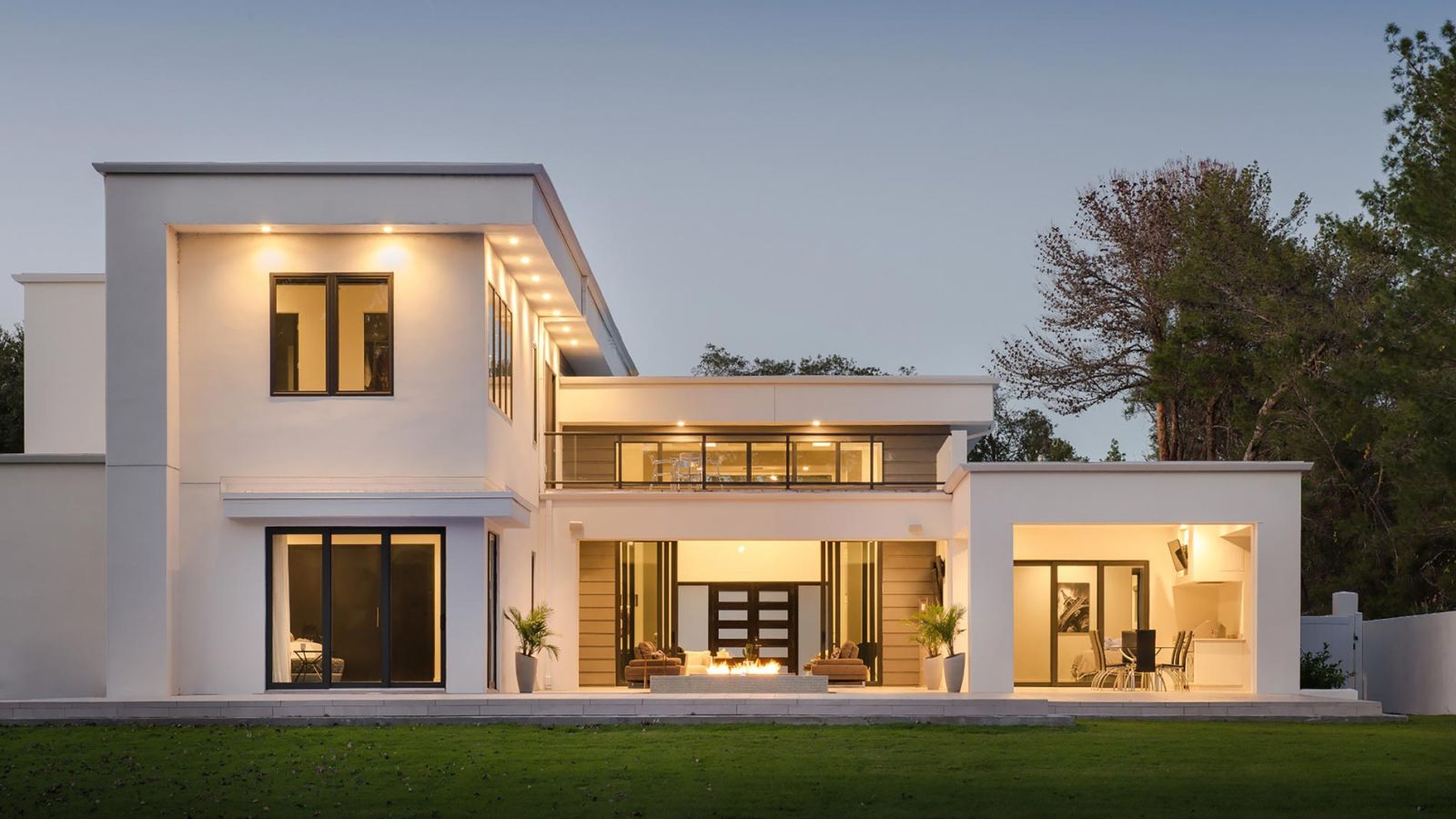 Modern white two-story home with outdoor lighting and open patio space
