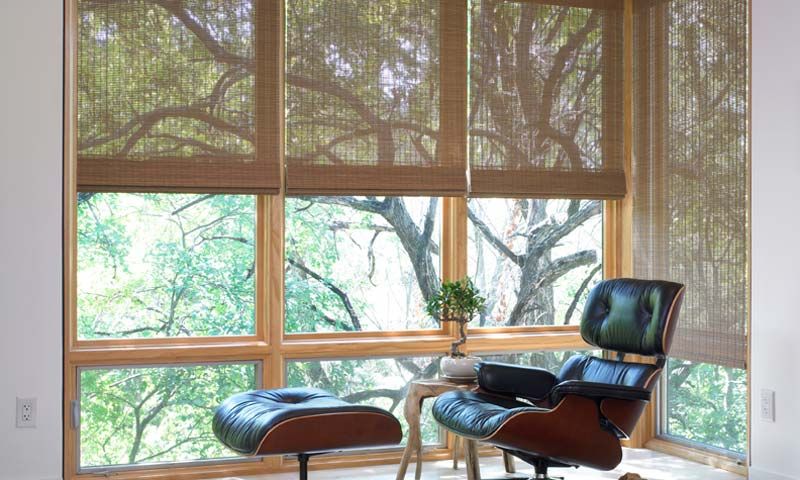 Tranquil sitting area with Lutron woven Roman shades, an Eames lounge chair, and a view of the trees outside.