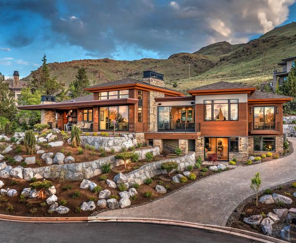 Modern hillside home with large windows, stone accents, and landscaped rock garden at sunset.